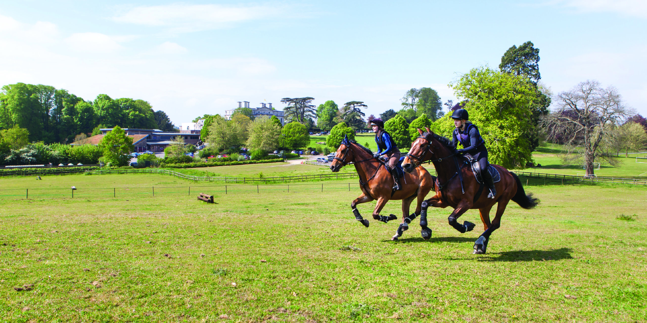 Two Equine students riding across field, with the Main House in the background